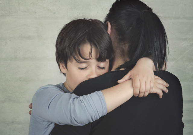 Young male child with eyes closed and woman, embracing.